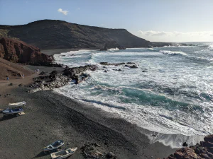 beach on Lanzarote with dark volcanic mountains and some small boats