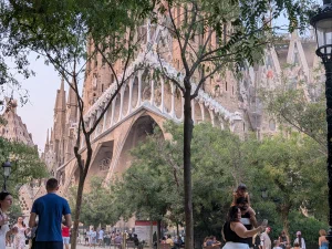 The Sagrada Familia seen through trees from a nearby park, with visitors walking below