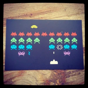 A Space Invaders postcard on a wooden surface
