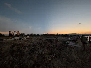 A beach at dusk with the eclipsed sun low on the horizon, people watching from the sand under an orange and blue sky